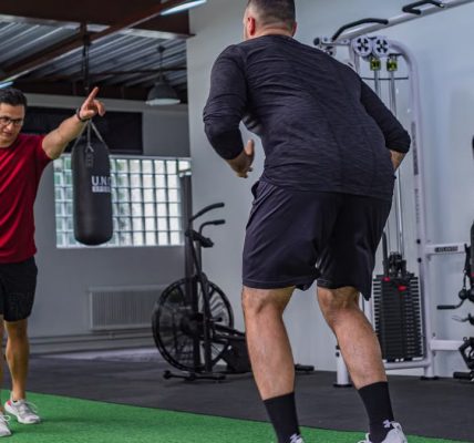 Back view of muscular man in sportswear doing exercises with trainer in modern fitness club