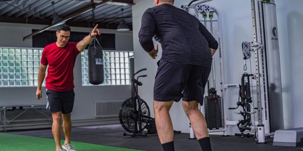 Back view of muscular man in sportswear doing exercises with trainer in modern fitness club